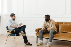 a male therapist sits in a chair and listens to male patient who is sitting on a couch in his marijuana addiction treatment program